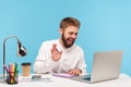 Happy smiling man office worker sitting at workplace with notepad and pencil, saying hi talking video call on laptop, holding Royalty Free Stock Photo