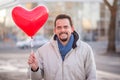 Happy smiling man standing with closed eyes and holding with  red heart-shaped air balloon. Date and Valentines day concept Royalty Free Stock Photo