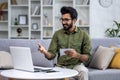 Happy and smiling man studying remotely sitting on sofa in living room, Hispanic man talking on video call using laptop Royalty Free Stock Photo