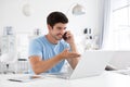 Happy smiling man works on his laptop and talking phone at home. Cheerful freelance Royalty Free Stock Photo