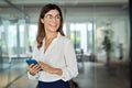 Happy smiling mature business woman holding phone looking away in office. Royalty Free Stock Photo