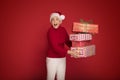 Mature woman in red santa claus hat holding stack of gift boxes, on red studio background. Christmas shopping, copy Royalty Free Stock Photo