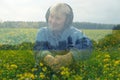 Happy smiling mature woman sitting wearing headphones and listen to relaxation music on field with alot of yellow flowers. Double