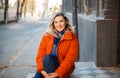 Happy smiling middle aged woman in orange down jacket sitting on concrete stairs outdoors Royalty Free Stock Photo