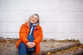 Happy smiling middle aged woman in orange down jacket sitting on concrete stairs outdoors Royalty Free Stock Photo