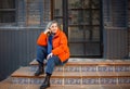 Happy smiling middle aged woman in orange down jacket sitting on concrete stairs outdoors Royalty Free Stock Photo