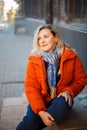 Happy smiling middle aged woman in orange down jacket sitting on concrete stairs outdoors Royalty Free Stock Photo