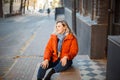 Happy smiling middle aged woman in orange down jacket sitting on concrete stairs outdoors Royalty Free Stock Photo