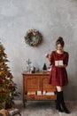 Happy smiling model girl in plaid red dress holding the present box and posing near Christmas tree. Young beautiful Royalty Free Stock Photo