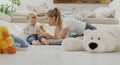 Happy and smiling mom with child baby playing with wooden toys and plush stuffed animals, at home sitting on floor with pillows, Royalty Free Stock Photo