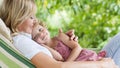 Happy and smiling mom hugs her little girl daughter child blue eyes with blond curly hair, together lying on the hammock in the Royalty Free Stock Photo
