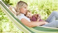 Happy and smiling mom hugs her little girl daughter child blue eyes with blond curly hair, together lying on the hammock in the Royalty Free Stock Photo