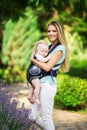 Happy smiling mother with baby boy in sling walking in green park Royalty Free Stock Photo