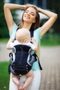 Happy smiling mother with baby boy in sling walking in green park Royalty Free Stock Photo