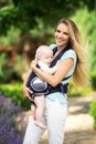 Happy smiling mother with baby boy in sling walking in green park Royalty Free Stock Photo