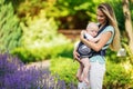 Happy smiling mother with baby boy in sling walking in park Royalty Free Stock Photo