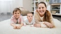 Happy smiling mother with baby and older son lying on soft carpet at living room. Parenting, children happiness and Royalty Free Stock Photo