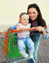Happy smiling mother and child with shopping bags and trolley cart walking in city Royalty Free Stock Photo
