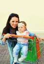 Happy smiling mother and child with shopping bags and trolley cart walking in the city Royalty Free Stock Photo