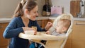 Happy smiling mother feeding her baby son with fruit porridge at kitchen. Concept of parenting, healthy nutrition and baby care Royalty Free Stock Photo