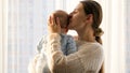 Happy smiling mother hugging and kissing her little baby son at big window in living room. Concept of family happiness Royalty Free Stock Photo