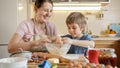 Happy smiling mother with little son kneading and smelling dough in glass bowl. Children cooking with parents, little