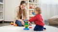 Happy smiling mother looking at her little baby son assembling toy pyramid or tower. Baby development, child playing games, Royalty Free Stock Photo