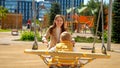 Happy smiling mother rocking her baby son swinging in swing on playground. Children playing outdoor, kids outside, summer holiday Royalty Free Stock Photo