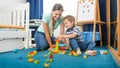 Happy smiling mother sitting on floor with her little son and playing with colorful constructro blocks Royalty Free Stock Photo