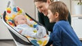 Happy smiling mother sitting on floor next to her older son and little baby boy rocking in electric chair. Child Royalty Free Stock Photo