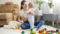 Happy smiling mother supporting her little baby son and teaching walking on carpet in living room. Concept of children Royalty Free Stock Photo