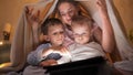 Happy smiling mother with two sons in pajamas having fun on bed and playing games on tablet computer. Family having time together Royalty Free Stock Photo