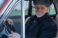 Happy smiling old man in black jacket driving retro car, holds her hands on wheel and looking at the camera Royalty Free Stock Photo