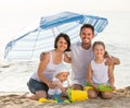 Family sitting under umbrella on the beach. Royalty Free Stock Photo