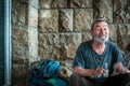 Happy and smiling poor homeless man sitting in the shadow of the building on the urban street in the city