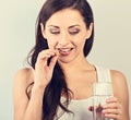 Happy smiling positive woman eating the pill and holding the glass of water in the hand on blue background. Closeup Royalty Free Stock Photo