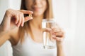 Happy smiling positive woman eating the pill and holding the glass of water in the hand, in her home Royalty Free Stock Photo
