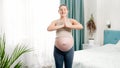 Happy smiling pregnant woman with big belly standing at big window and doing yoga exercises and positions. Concept of Royalty Free Stock Photo