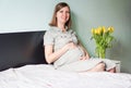 Happy smiling pregnant woman sitting on a bed in a bedroom at home and touching her belly. Royalty Free Stock Photo