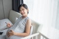 Happy Smiling Asian Pregnant woman sitting on bed touching her belly and holding ultrasound scan photo. Mother with sonogram of Royalty Free Stock Photo