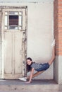 Happy smiling preteen girl do gymnastics in the doorway next to old wooden door in brick and concrete wall. Outdoor dance