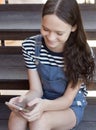 Happy smiling preteen girl sitting on stairs and chatting on the phone. Top view lifestyle shot. Technology generation