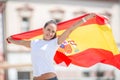 Happy smiling pretty girl holds a flag of Spain behind her celebrating on a street