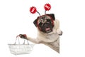 Happy smiling pug puppy dog, holding up shopping basket, wearing diadem with red sale sign Royalty Free Stock Photo