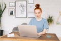 Happy smiling redhead young woman student is working on laptop computer at the desk at home office. Royalty Free Stock Photo