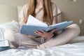 Happy and smiling relaxed cheerful woman reading note book and working from home office on bed and drinking coffee. Blonde girl Royalty Free Stock Photo