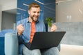 happy smiling remote online working man in casual outfit with laptop in joyful successful winning gesture sitting in an