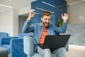 happy smiling remote online working man in casual outfit with laptop in joyful successful winning gesture sitting in an