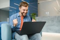 happy smiling remote online working man in casual outfit with laptop in joyful successful winning gesture sitting in an