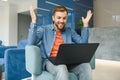 happy smiling remote online working man in casual outfit with laptop in joyful successful winning gesture sitting in an